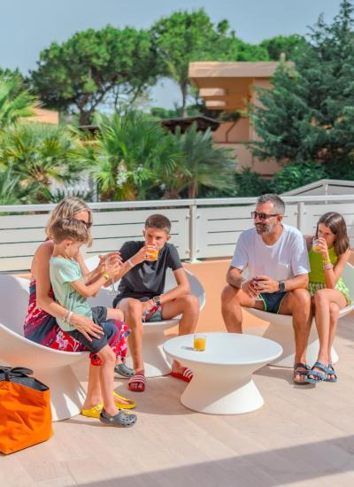 Familie trinkt Saft auf sonniger Terrasse, umgeben von Bäumen.