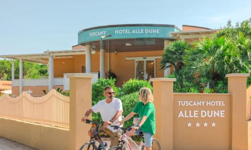 Zwei Personen fahren Fahrrad vor dem Tuscany Hotel Alle Dune.