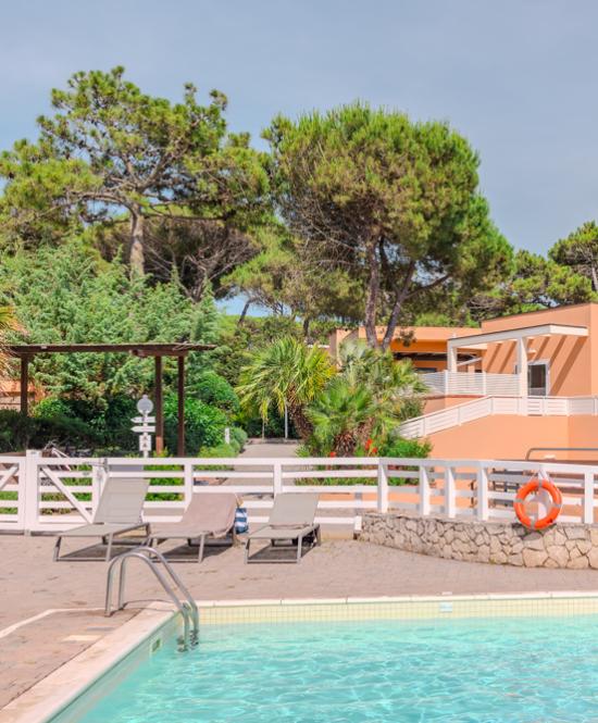 Outdoor pool with loungers, lush greenery, and peach-colored villas.