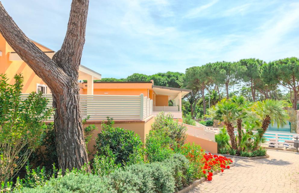 Villa con giardino, palme e fiori rossi in una giornata soleggiata.